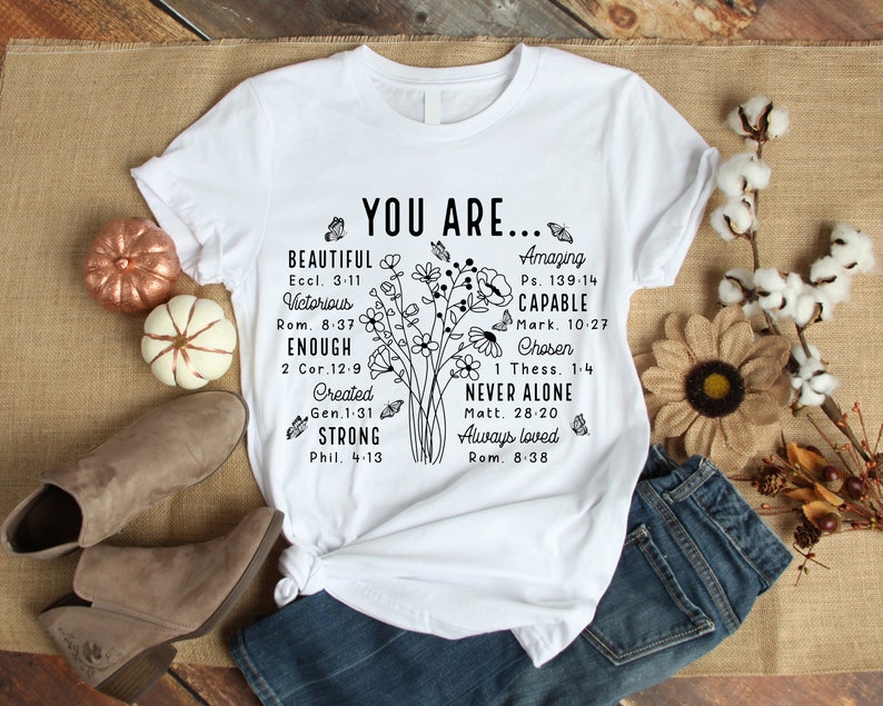 May include: White t-shirt with black text and floral design. The text reads "You are... Beautiful, Victorious, Enough, Created, Strong" and "Amazing, Capable, Chosen, Never Alone, Always Loved".