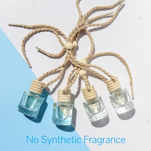 May include: Five small glass bottles with blue liquid and wooden tops are hanging from beige and gold cords. The bottles are labeled "No Synthetic Fragrance".