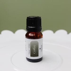 以下が含まれることがあります： 黒い蓋が付いた小さな茶色のガラス瓶。ラベルには「Coffee Luca + Grey」と、小さな白いカエデの葉のロゴが書かれています。