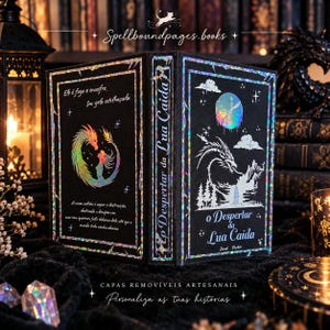 May include: A black book with holographic foil details featuring a dragon and a person on the cover. The front cover displays the title O Despertar da Lua Caída, a mountain landscape, and a moon. The back cover includes text and a circular dragon design.