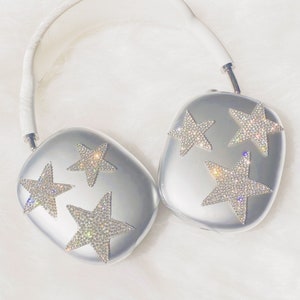 以下が含まれることがあります： 白いヘッドバンドと各イヤーカップに星形のデザインが施されたシルバーのヘッドホン。星はラインストーンでできています。