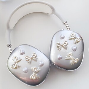 May include: White and silver headphones with a white headband and silver earcups. The earcups are decorated with white bows and hearts.