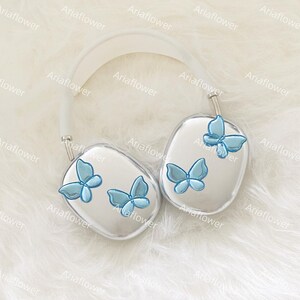 Peut inclure: Casque audio argent&eacute; avec un bandeau blanc et des oreillettes orn&eacute;es de papillons bleu clair. L'ensemble est pos&eacute; sur un fond blanc et duveteux, cr&eacute;ant une esth&eacute;tique &eacute;pur&eacute;e et &eacute;l&eacute;gante.
