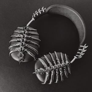 May include: Black headphones with a skeletal design on the earcups. The headphones have a black headband with a silver accent.