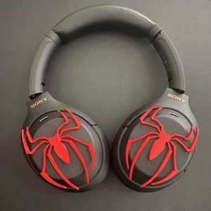 May include: Black wireless headphones with a red spider-man logo on each earcup. The headphones have the word "SONY" written in gold on each earcup.