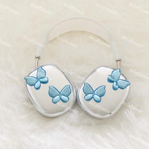 Peut inclure: Casque audio argent&eacute; orn&eacute; de papillons bleu clair. Les &eacute;couteurs pr&eacute;sentent des motifs de papillons en trois dimensions. L'arceau est blanc. Design moderne et &eacute;l&eacute;gant. Le texte "Ariaflower" est r&eacute;p&eacute;t&eacute; dans l'image.