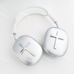 May include: White headphones with silver earcups featuring a raised cross design. The headphones have a white headband.