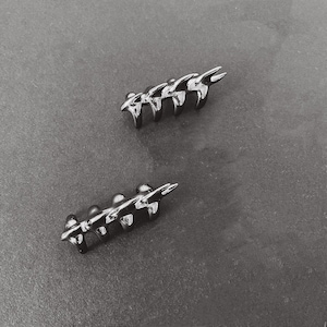 May include: Two silver-toned, open-ended, ring-like objects with a jagged, pointed design. The objects are made of metal and have a shiny finish.