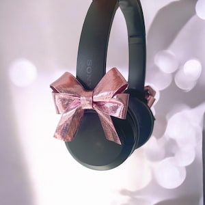 May include: Black over-ear headphones with a pink bow tied around the earcups. The headphones have the word "SONY" printed on the side.