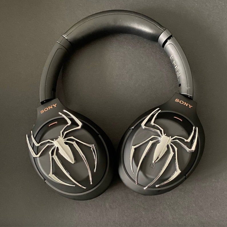 May include: Black wireless headphones with a silver spider-man logo on each earcup. The headphones have a black headband and the word "SONY" is printed on each earcup.