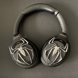 May include: Black wireless headphones with a silver spider-man logo on each earcup. The headphones have a black headband and the word "SONY" is printed on each earcup.