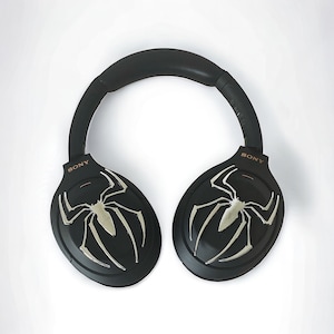 May include: Black over-ear headphones with a spider web design on each earcup. The headphones have the word "SONY" printed on each earcup.