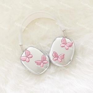 Peut inclure: Casque audio argent&eacute; avec un arceau blanc et des oreillettes orn&eacute;es de papillons roses. L'ensemble est pos&eacute; sur un fond blanc doux et textur&eacute;, cr&eacute;ant une esth&eacute;tique &eacute;pur&eacute;e et &eacute;l&eacute;gante.