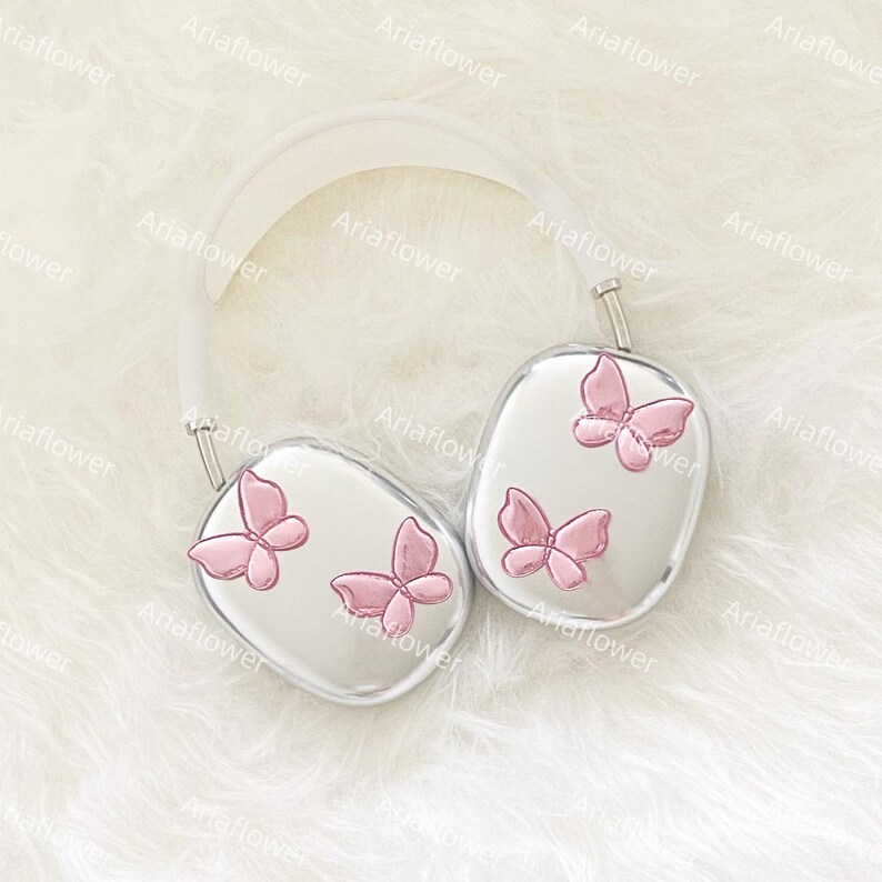 Peut inclure: Casque audio argent&eacute; avec un arceau blanc et des oreillettes orn&eacute;es de papillons roses. L'ensemble est pos&eacute; sur un fond blanc doux et textur&eacute;, cr&eacute;ant une esth&eacute;tique &eacute;pur&eacute;e et &eacute;l&eacute;gante.