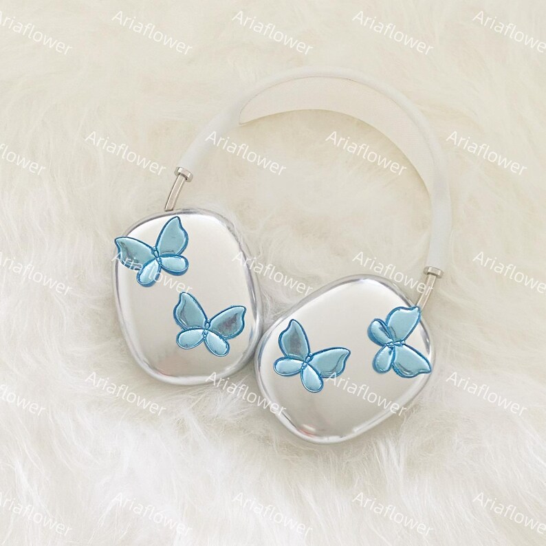 Peut inclure: Casque audio argent&eacute; avec un bandeau blanc et des papillons bleus clairs. Les &eacute;couteurs ont une surface r&eacute;fl&eacute;chissante, chacun avec deux ou trois d&eacute;corations de papillons. Le casque repose sur une surface blanche et duveteuse.