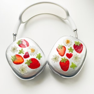 May include: White headphones with a floral design featuring pressed strawberries and flowers. The headphones are made of a smooth, white material and have a minimalist design.