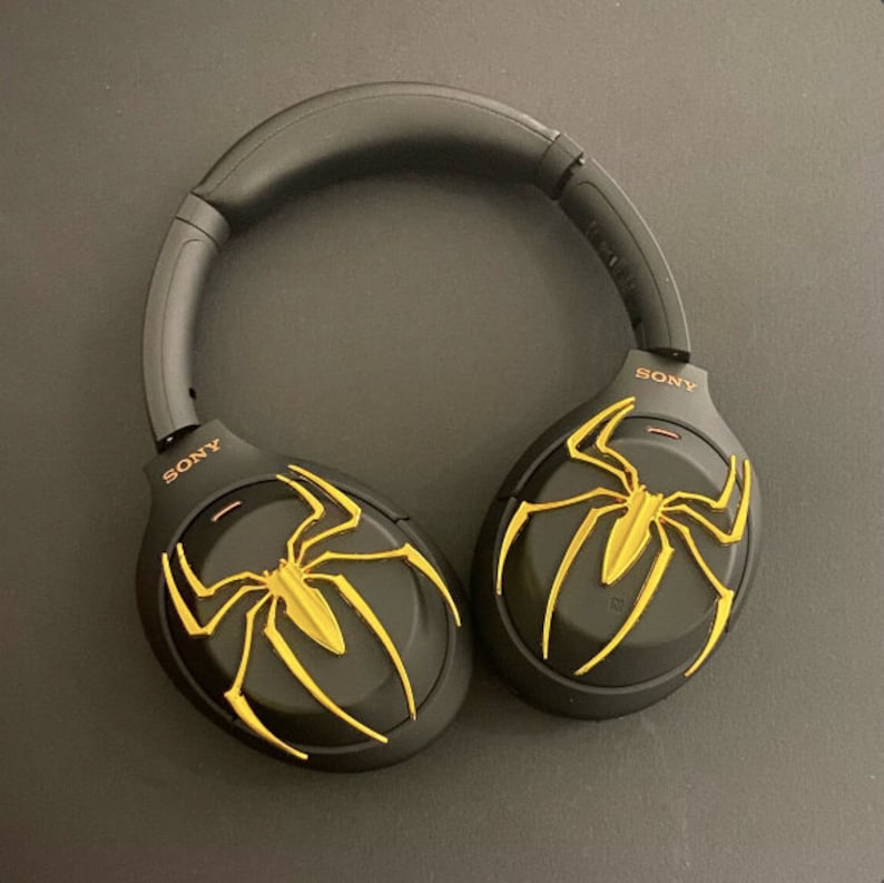 May include: Black wireless headphones with a gold spider web design on each earcup. The headphones have the word "SONY" printed on each earcup.
