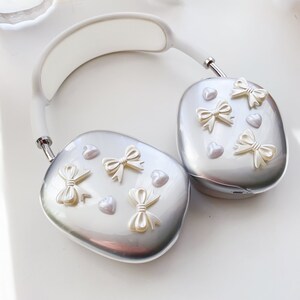 May include: White and silver headphones with a white headband and silver earcups. The earcups are decorated with white bows and hearts.