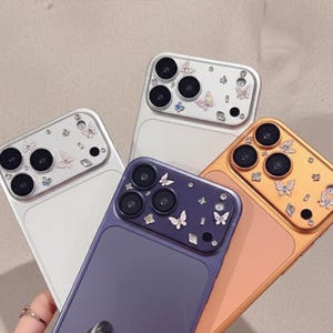 Op de afbeelding: Een verzameling kleurrijke telefoonhoesjes met vlinderversieringen. De hoesjes zijn er in verschillende kleuren, waaronder zilver, paars en goud. De vlinderaccenten zijn in roze en witte tinten.