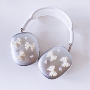 May include: White and silver over-ear headphones with a white headband and silver earcups. The earcups are decorated with white bows and hearts.
