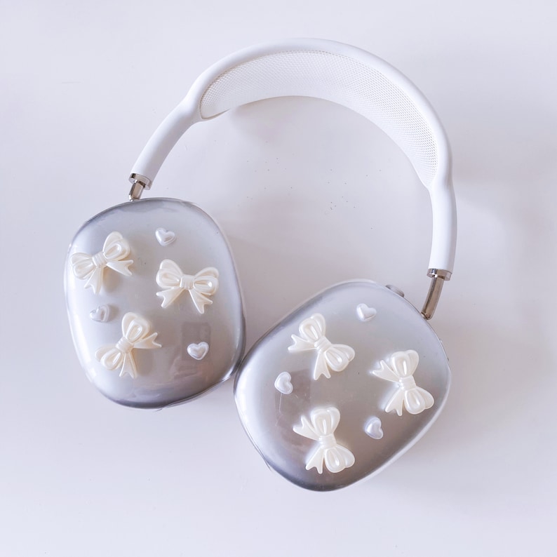 May include: White and silver over-ear headphones with a white headband and silver earcups. The earcups are decorated with white bows and hearts.
