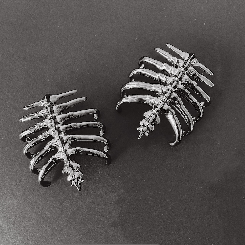 May include: Two silver skeleton ribcage hair clips. The clips are made of metal and have a detailed ribcage design.
