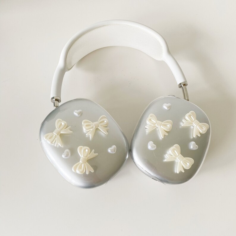 May include: White headphones with a silver finish and a white headband. The earcups are decorated with small white bows and hearts.