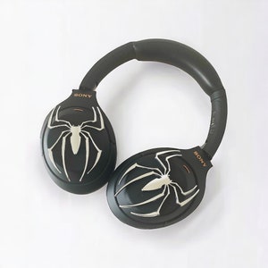 May include: Black wireless headphones with a spider web design on each earcup. The headphones have the word "SONY" printed on the right earcup.
