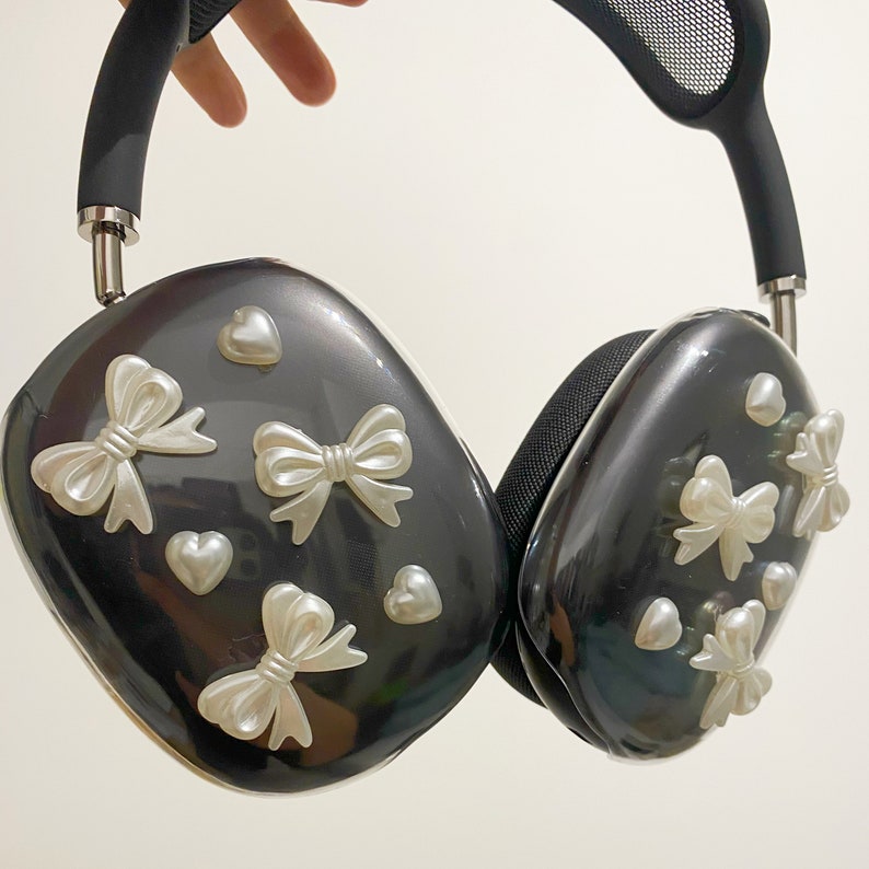 May include: Black headphones with a mesh headband and white bow accents. The headphones have a glossy finish and are decorated with small white hearts.