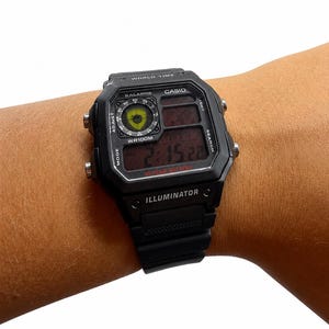 May include: A black digital wristwatch with a rectangular case and a black resin strap. The watch face features the text WORLD TIME, CASIO, 5 ALARMS, WR100M, 10 YEAR BATTERY, and ILLUMINATOR. A small circular analog display is visible in the top left corner.