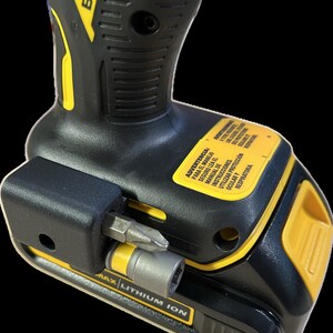 May include: A black and yellow power drill with a black and silver bit attached. The drill has a black handle with a yellow grip and a black battery pack with a yellow label that reads "MAX LITHIUM ION". The label also has a warning in Spanish that reads "ADVERTENCIA: PARA EL MANEJO SEGURO LEA EL MANUAL DE INSTRUCCIONES. UTILIZAR PROTECCIÓN OCULAR Y RESPIRATORIA."