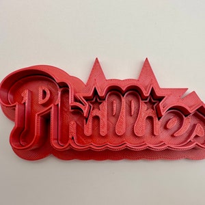 May include: Red plastic cookie cutter shaped like the word "Phipps" with two stars above the "P".