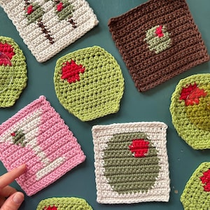 Könnte beinhalten: Ein Set aus acht gehäkelten Untersetzern mit verschiedenen Designs. Die Untersetzer sind aus verschiedenen Garnfarben gefertigt, darunter Weiß, Braun, Grün und Rosa. Jeder Untersetzer hat einen roten Kreis in der Mitte.