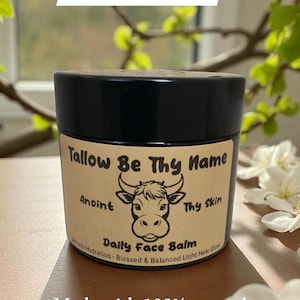 Könnte beinhalten: Ein Tiegel Daily Face Balm mit schwarzem Deckel und einem Etikett mit einer Kuh-Illustration. Auf dem Etikett steht "Tallow Be Thy Name" und "Hergestellt aus 100% natürlichen Inhaltsstoffen."
