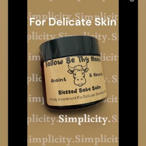 Könnte beinhalten: Ein Tiegel Blessed Babe Balm für empfindliche Haut. Das Etikett zeigt eine Kuh-Illustration und den Text "Tallow Be Thy Name" und "A Holy Anointment For Delicate Sensitive Skin". Der Tiegel ist schwarz mit einem braunen Etikett.