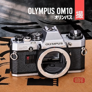 May include: An Olympus OM10 35mm film camera body with a silver and black finish. The front features the Olympus logo, OM10 model text, a lens mount, and strap lugs. The top includes various control dials and a hot shoe mount.