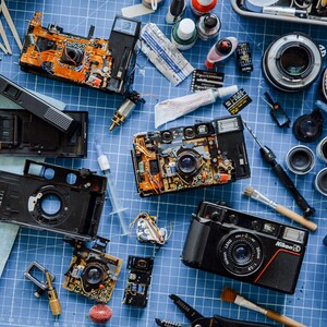 A busy Workbench with multiple disassembled L35 Nikon cameras, tools, film rolls, and various camera parts arranged together on worktop.