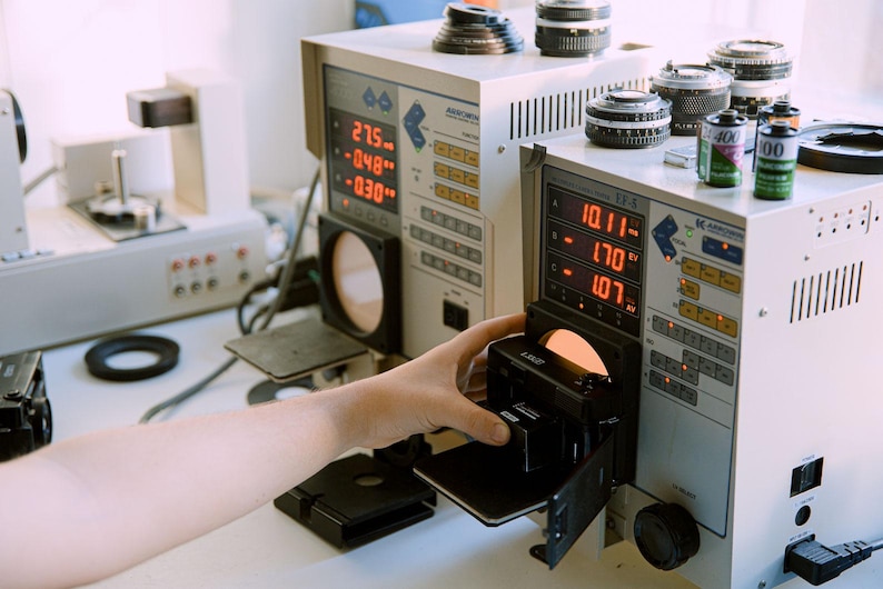 Nikon L35AD (Pikaichi) film camera being tested on a Kyoritsu Arrowin EF8000 with an adjacent EF-5 Shutter Tester, showing the equipment and testing process.