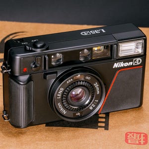 Front view of the Nikon L35AD (Pikaichi) film camera, facing above, showing the lens, graphics and built-in flash.