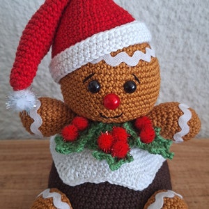 以下が含まれることがあります： 赤いサンタの帽子に白いポンポン、緑のヒイラギの葉と赤い実のついた白い編み物のマフラー、そして茶色の編み物のプディングの土台をつけた、編み物のジンジャーブレッドマンです。