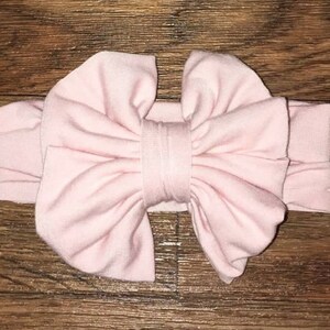 Peut inclure: Un bandeau en tissu rose pâle avec un grand nœud. Le bandeau est fait d'un matériau doux et extensible, parfait pour les nouveau-nés et les bébés.