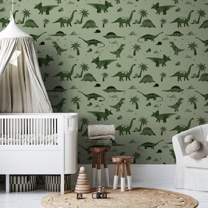 Op de afbeelding: Een babykamer met een groene dinosaurusbehang met een wieg, een hemelbed, een stoel en een speelgoedblokkentoren.