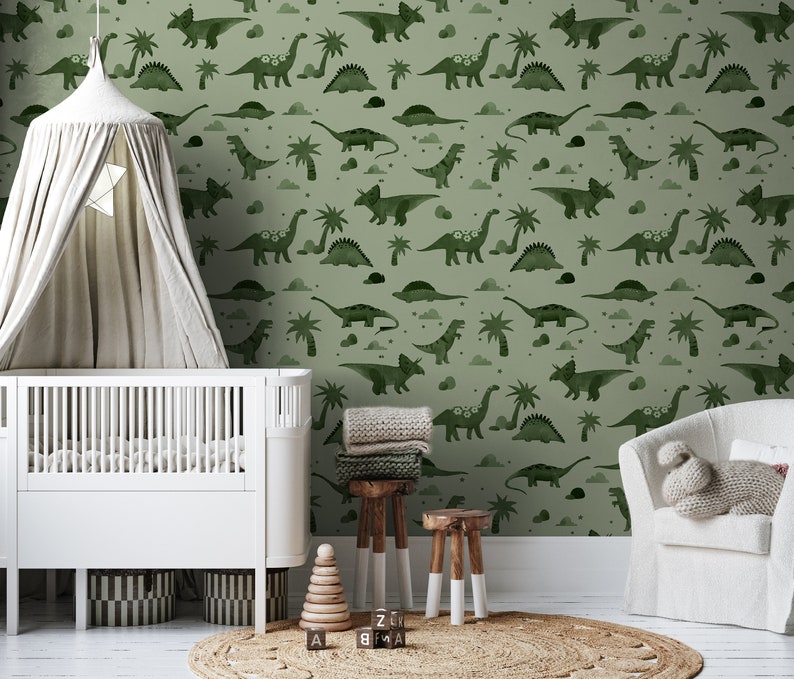 Op de afbeelding: Een babykamer met een groene dinosaurusbehang met een wieg, een hemelbed, een stoel en een speelgoedblokkentoren.