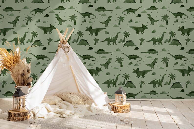 Op de afbeelding: Een groen-wit behang met een herhalend patroon van dinosaurussen, palmbomen en wolken. Op de voorgrond staat een witte tipi-tent met kussens en dekens erin.