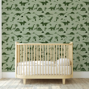 Op de afbeelding: Een babykamer met een wieg voor een muur met een groene dinosaurusbehang. Het behang heeft een herhalend patroon van dinosaurussen, palmbomen en wolken.