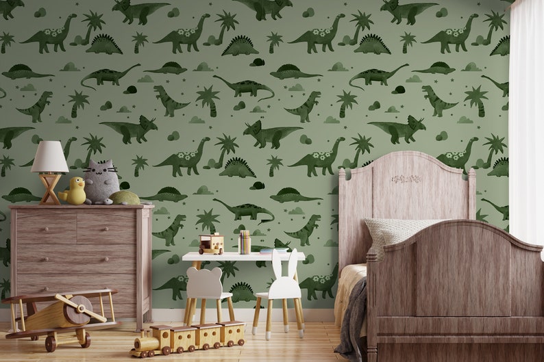Op de afbeelding: Een groen-wit behang met een herhalend patroon van dinosaurussen en palmbomen. Het behang is in een kinderkamer met een houten bed, een commode en speelgoed.