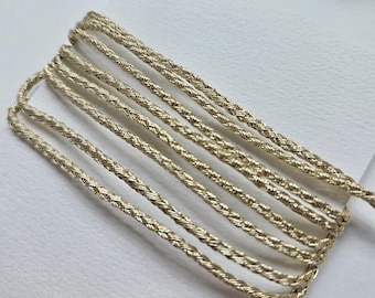 May include: Gold braided cord, a metallic trim for crafts and embellishments. The cord is shown in multiple strands, highlighting its texture and shine.