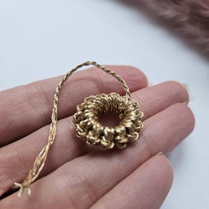 Op de afbeelding: Een gouden, gevlochten, ronde hanger met een touwachtige ketting.