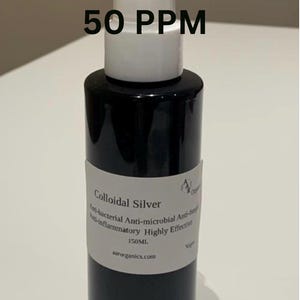 Op de afbeelding: Een zwarte cilindrische sprayfles met een witte pompdispenser. Het etiket bevat de tekst 50 PPM, Colloidal Silver, Anti-bacterial, Anti-microbial, Anti-fungal, Anti-inflammatory, Highly Effective, 150ML en aarorganics.com. De fles is ondoorzichtig zwart.