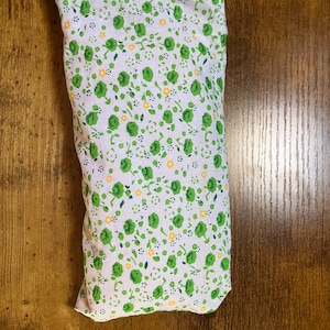 May include: A rectangular fabric pouch featuring a white background with a repeating pattern of small green floral clusters and tiny yellow accents. The textile item has a simple, folded construction with visible stitching along the top edge.